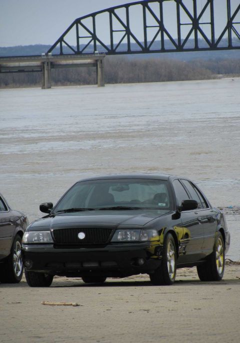 2003 Mercury Marauder - A black 2003 Mercury Marauder is parked on a sandy bank next to a body of water with a bridge in the background.
