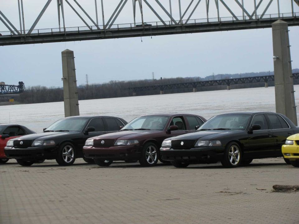 Four Mercury Marauders parked in a row near a bridge and river