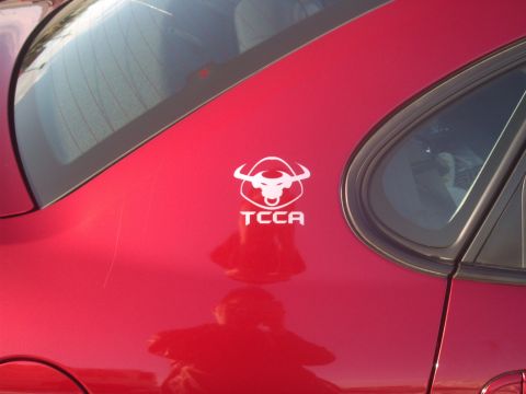 2000 Ford Taurus - A red car's side panel displays a white bull logo with the text 'TCCA' and a reflection of the photographer.