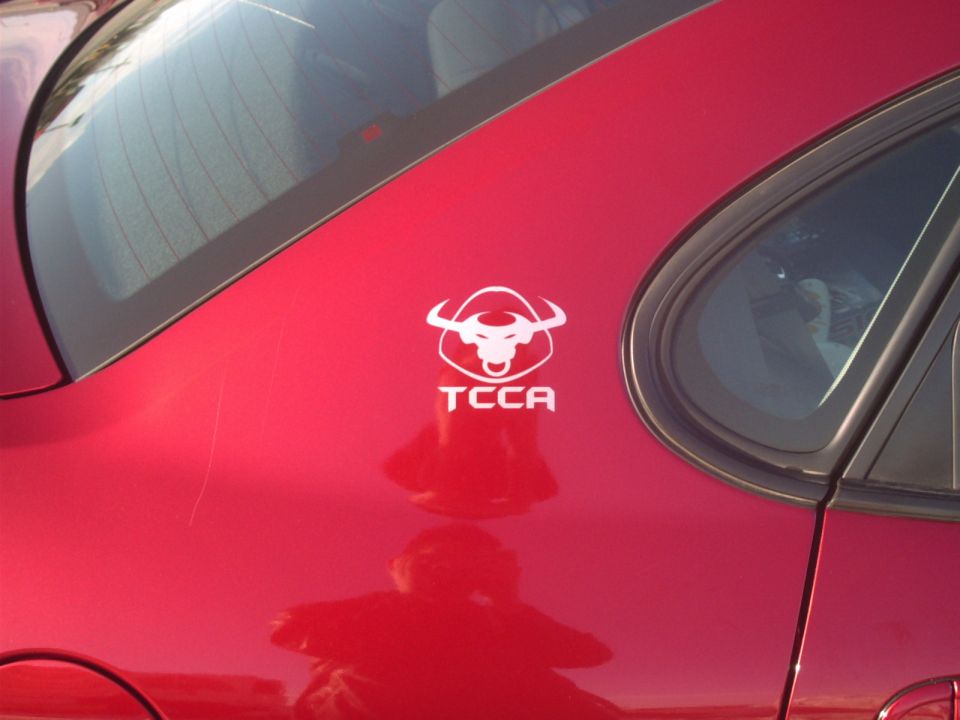Red car side panel with a white bull logo and 'TCCA' text, showing scratches and a reflection