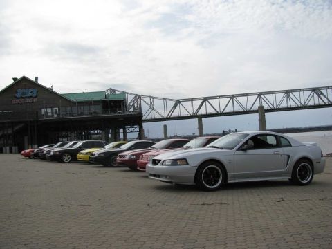 2003 Mercury Marauder - A line of Ford Mustangs are parked in front of a waterfront building under a cloudy sky.