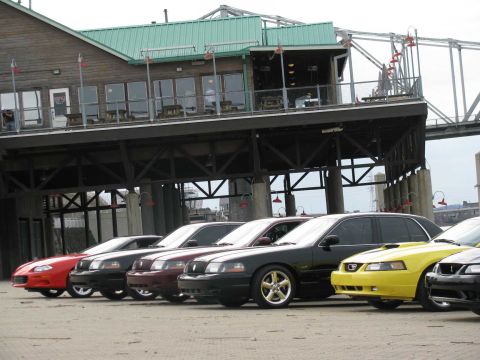 2003 Mercury Marauder - A row of sedans, including a black 2003 Mercury Marauder, are parked near a waterfront building.