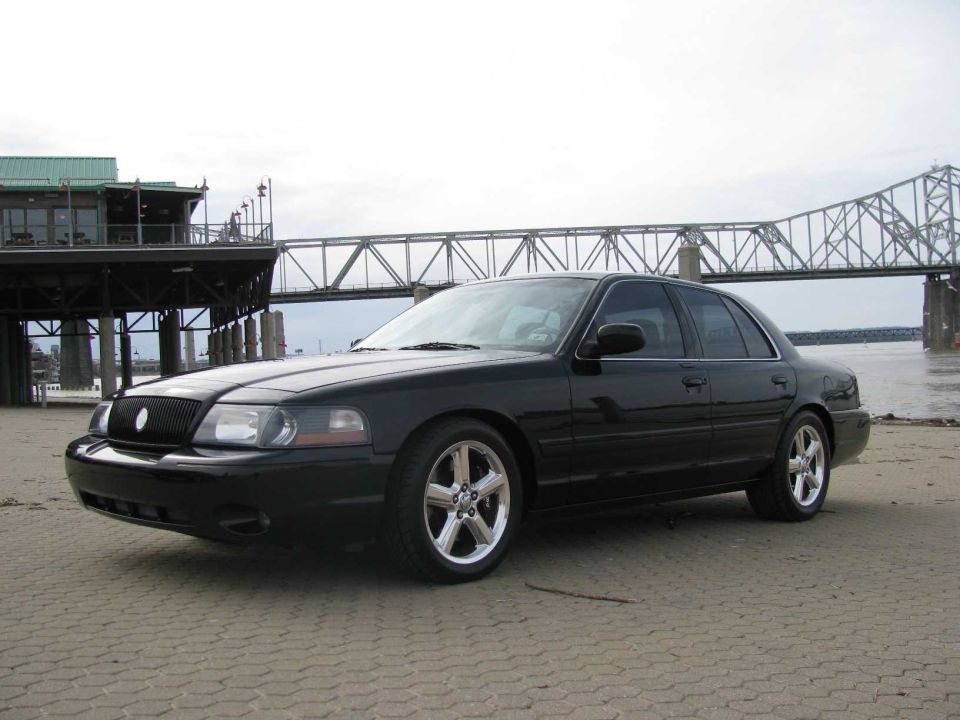 Black sedan parked on a paved area near a bridge and a building