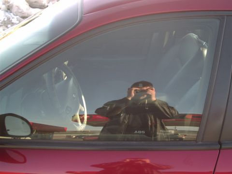 2000 Ford Taurus - Reflection of a person with a camera is visible in the window of a red car, showing the interior and a side mirror.