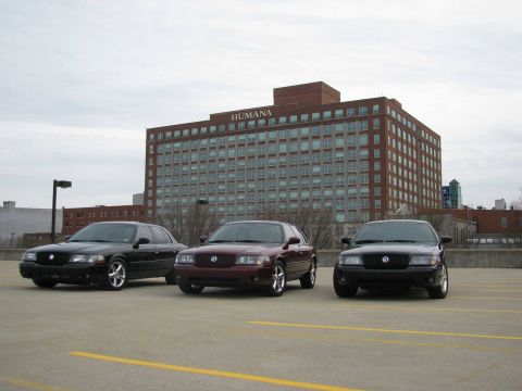 2003 Mercury Marauder - Three Mercury Marauders are parked in a lot, with a large brick building labeled 'HUMANA' behind them.
