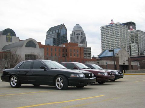 2003 Mercury Marauder - Three sedans, including a black 2003 Mercury Marauder, are parked in a lot with a city skyline behind them.
