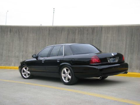 2003 Mercury Marauder - A black sedan with custom wheels is parked outdoors next to a concrete barrier.