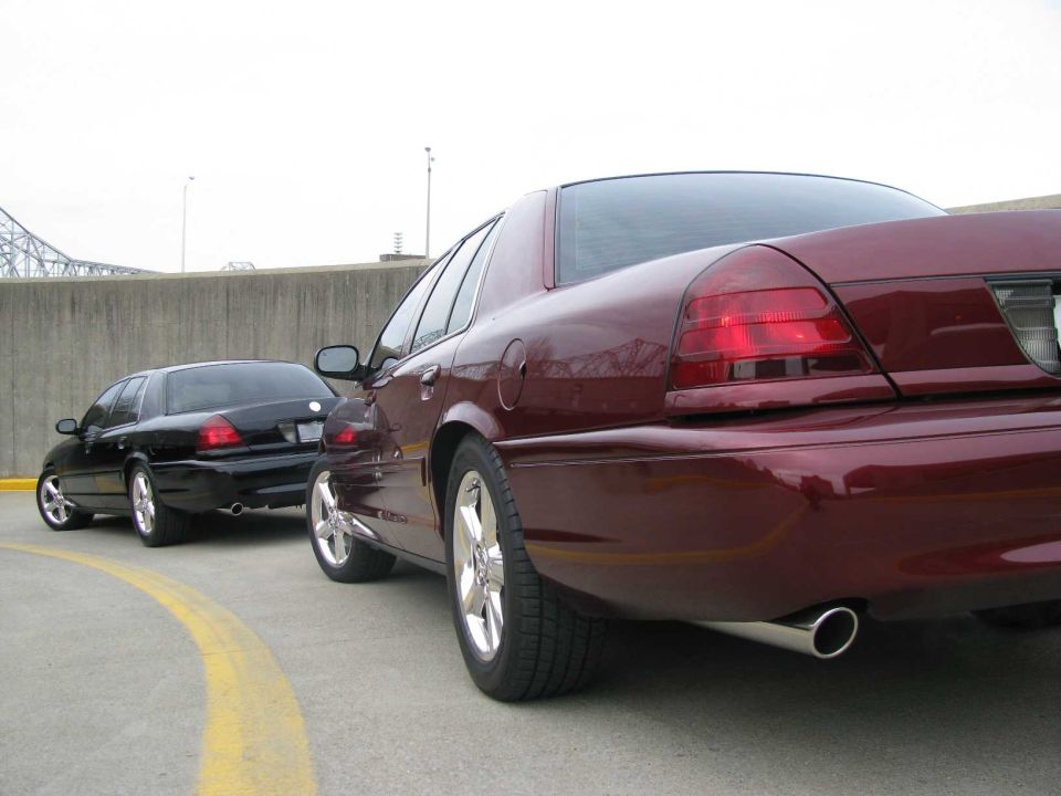 Maroon 2003 Mercury Marauder and black sedan parked on asphalt with yellow line, rear view
