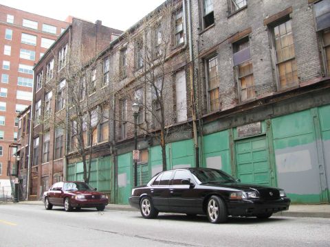 2003 Mercury Marauder - Two sedans, including a black 2003 Mercury Marauder, are parked on a city street next to weathered brick buildings.