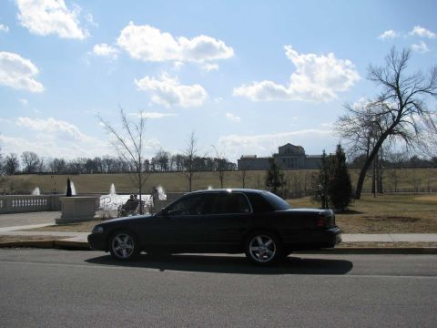 2003 Mercury Marauder - A dark sedan is parked on the street with a large building and fountains visible in the distance.