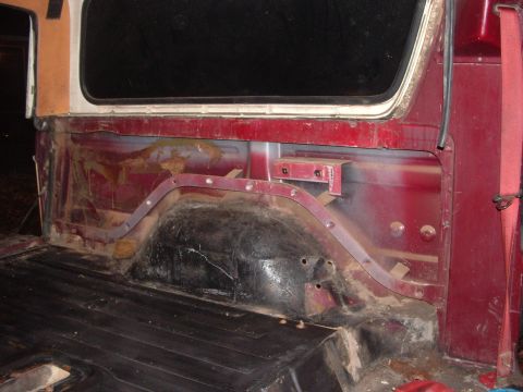 1979 Ford Bronco - The rear interior of a red vehicle is visible, with a black floor and exposed metal.