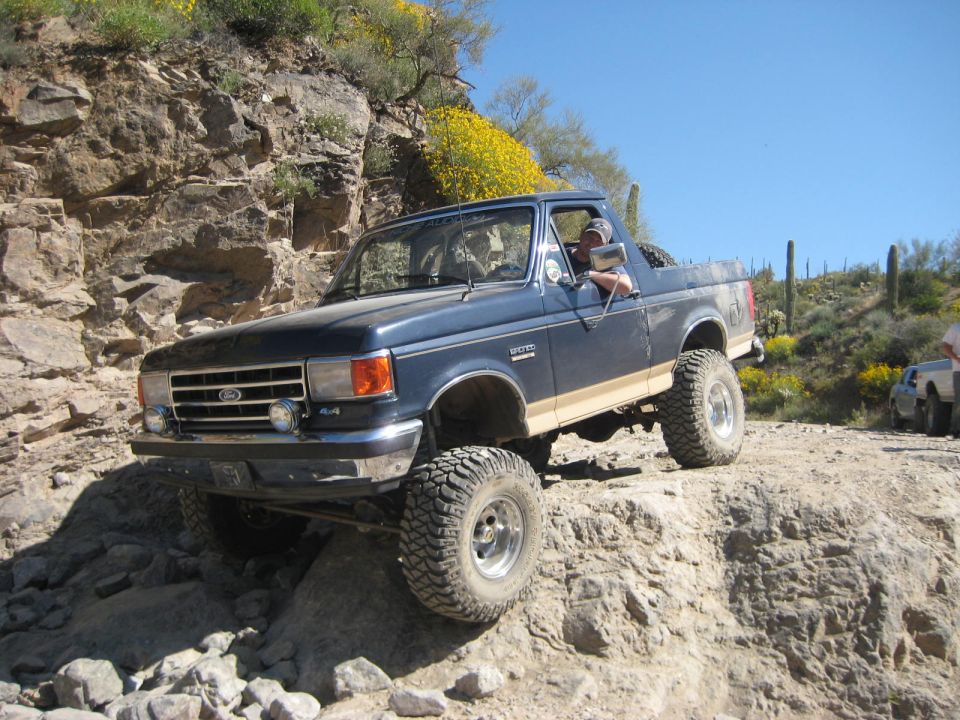 Blue Ford Bronco with tan stripe climbing rocks, driver visible
