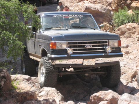 1991 Ford Bronco - Modified Ford F-Series truck tackling a challenging rocky trail. The vehicle has aftermarket wheels and tires.