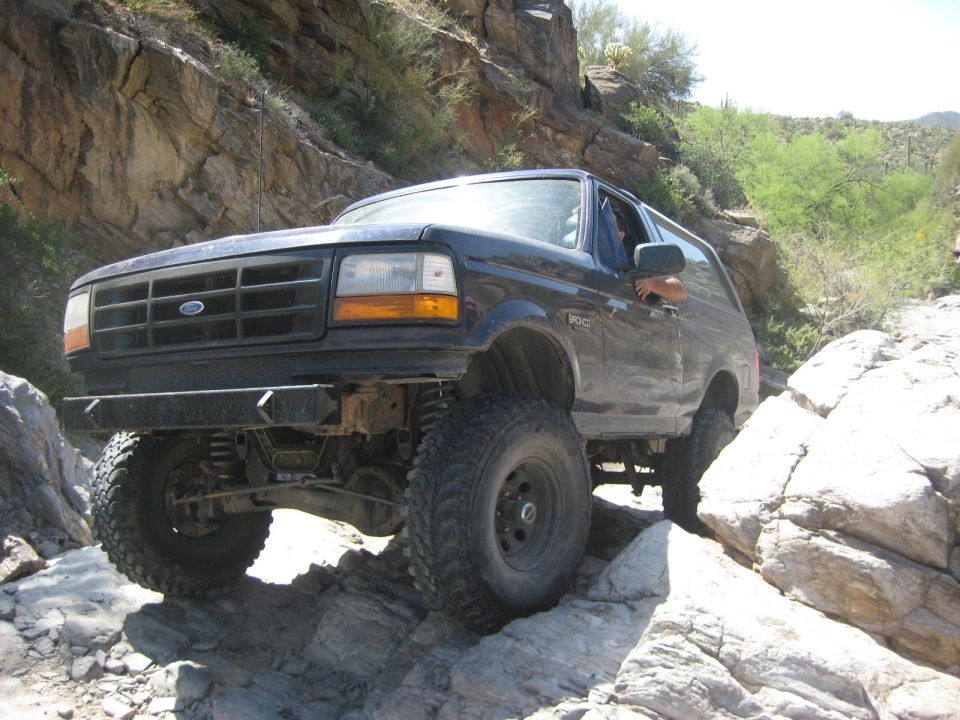 Dark blue Ford Bronco with lifted suspension and off-road tires navigating a rocky trail