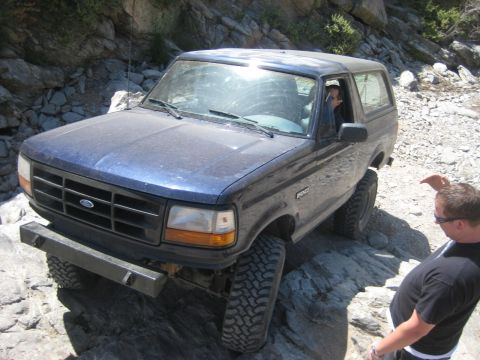 1991 Ford Bronco - A blue 1991 Ford Bronco navigates a rocky off-road trail with a driver and spotter present.