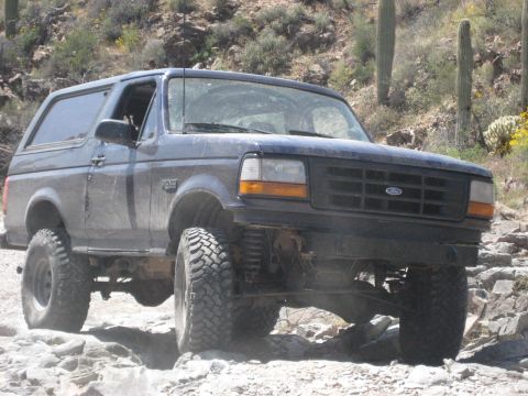 1991 Ford Bronco - A dark blue Ford Bronco navigates a challenging rocky terrain in a desert environment.