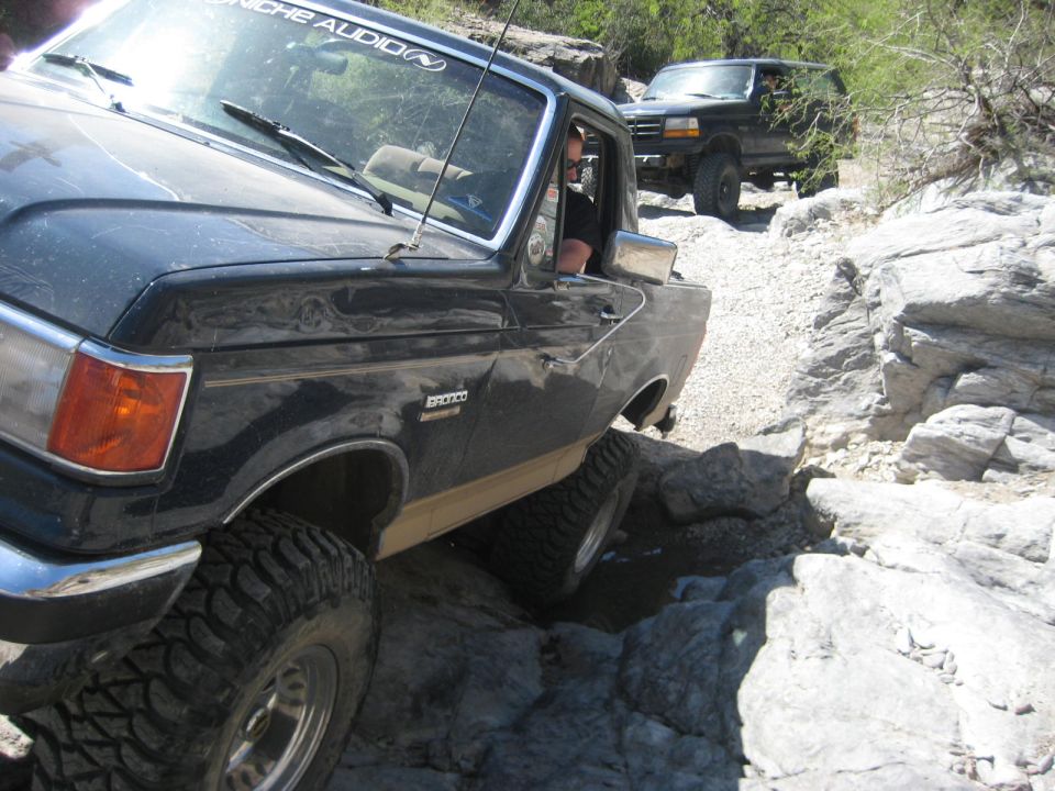 Black 1991 Ford Bronco on rocky trail, front 3/4 view. Another Bronco follows