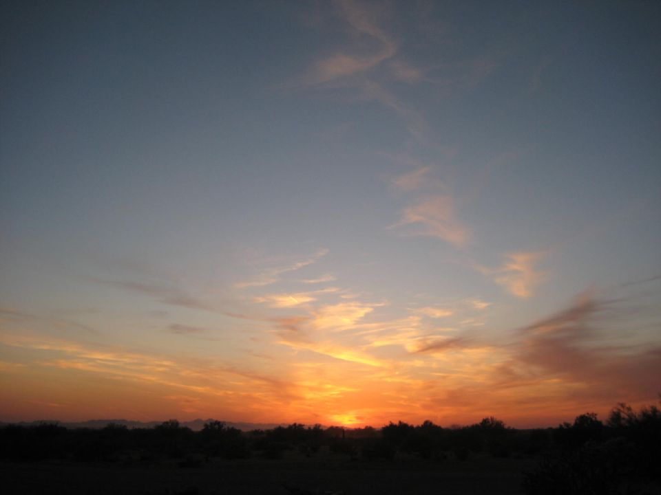 Sunset with orange and pink clouds over a dark desert horizon. Supermotors.net logo in the corner