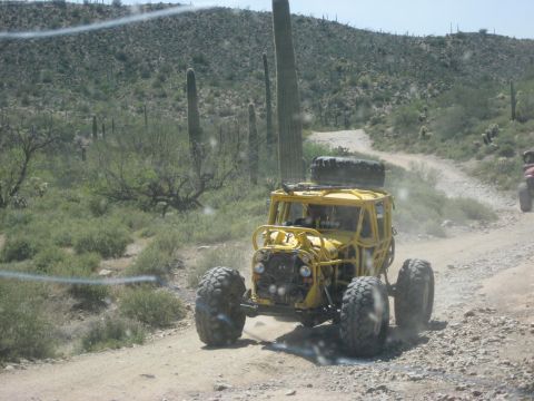 1991 Ford Bronco - A yellow buggy kicks up dust on a desert trail, with another vehicle visible in the distance.