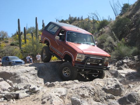 1991 Ford Bronco - Off-road adventure in the desert with a lifted Ford Bronco navigating a challenging rocky trail.