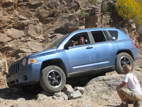 1991 Ford Bronco - A blue Jeep Compass navigates a rocky off-road trail with a driver and observer present.