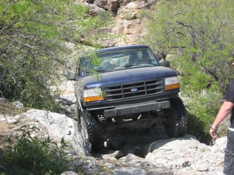 1991 Ford Bronco - A blue Ford Bronco tackles a challenging rocky trail, demonstrating its off-road capability.