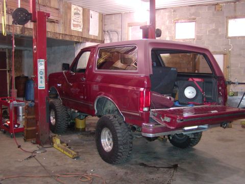 1991 Ford Bronco - Maroon Ford Bronco with lifted suspension and large tires is in a garage with its rear hatch open.