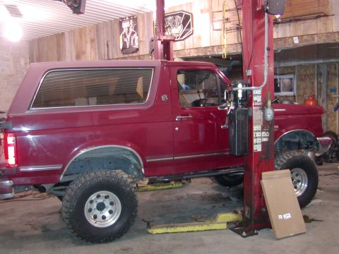 1991 Ford Bronco - A red 1991 Ford Bronco is shown on a vehicle lift in a garage setting.