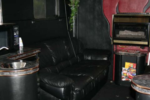 1993 Ford C-350 (Centurion Conversions) - The interior of a race trailer features a black leather couch, a sink, a microwave, and a fireplace.