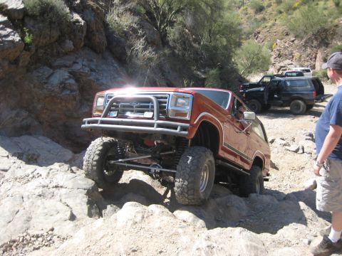 1991 Ford Bronco - Orange Ford Bronco tackling a challenging rocky trail with other vehicles in the background.