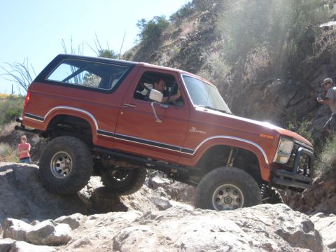 1991 Ford Bronco - This lifted Ford Bronco navigates a rocky off-road course under a bright sky.