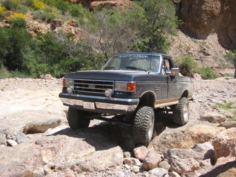 1991 Ford Bronco - A lifted Ford F-Series truck navigates a rocky, off-road path in a canyon.