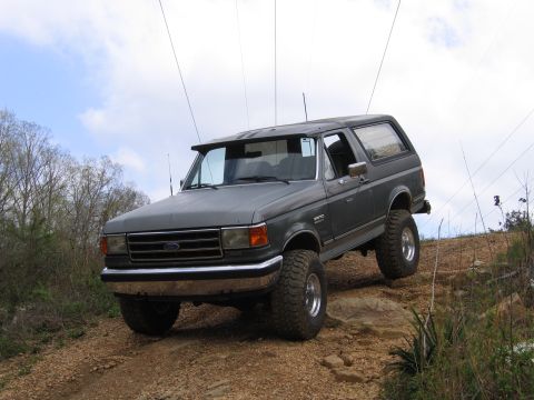 1989 Ford Bronco - A gray Ford Bronco navigates a challenging rocky terrain with its suspension lifted.