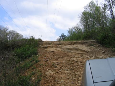 1989 Ford Bronco - A silver SUV navigates a challenging rocky path, with power lines overhead and trees lining the sides.