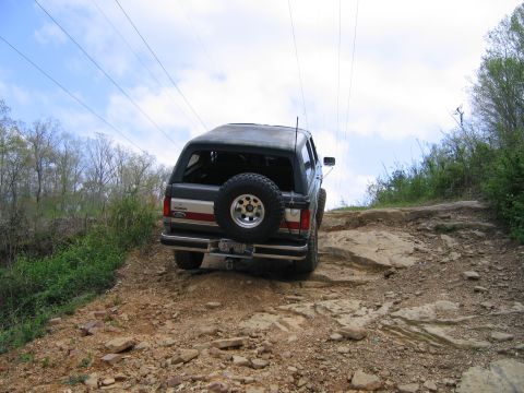 1989 Ford Bronco - A Ford Bronco navigates a challenging rocky terrain under a cloudy sky.