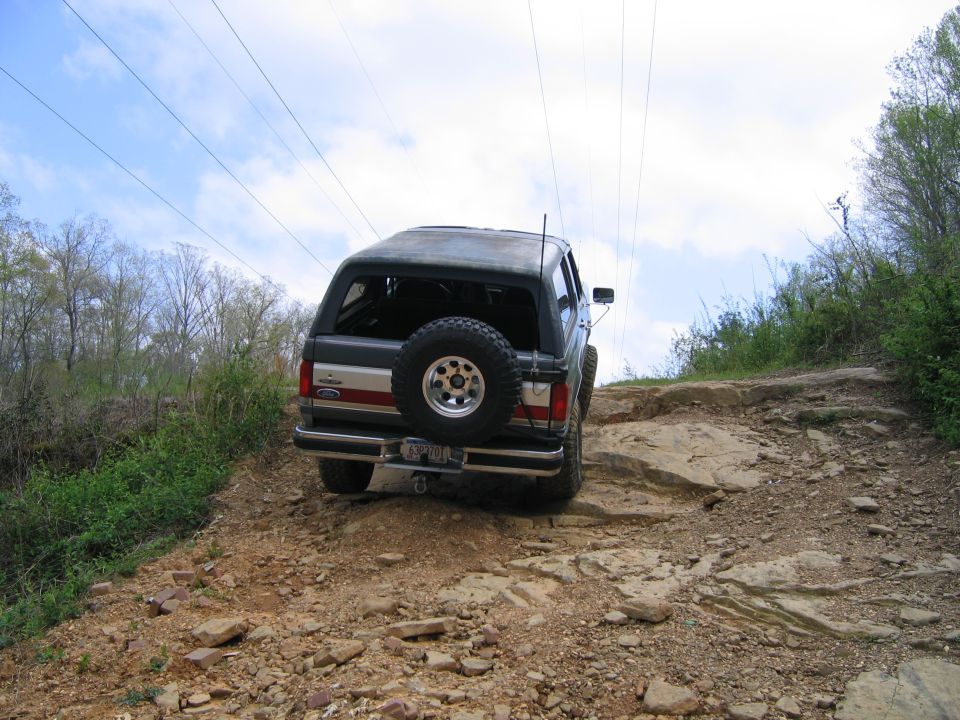 Bronco driving up rocky trail, spare tire on back