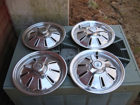 1964 Chevrolet Corvette - Set of four chrome hubcaps, each the iconic Corvette flags emblem, are displayed on an outdoor unit.