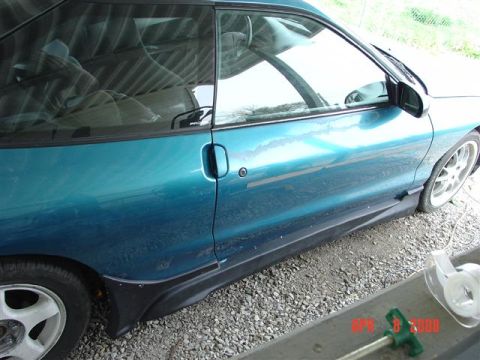 1993 Ford Probe - A teal coupe is parked on a gravel surface, showing its side profile and part of the interior.