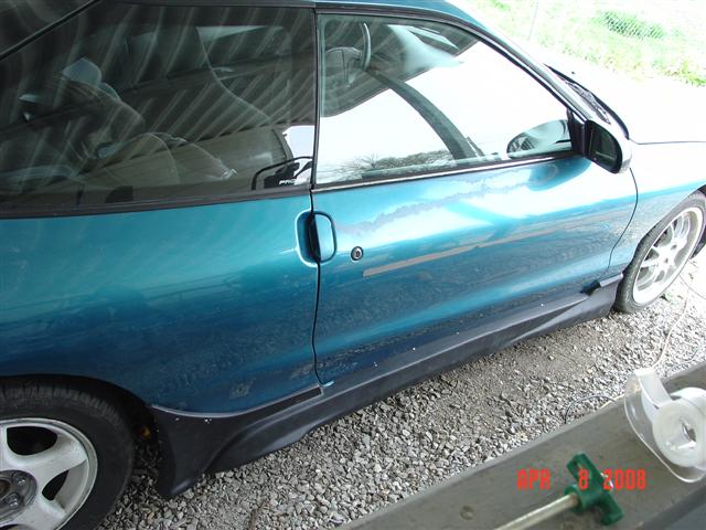 Side view of a teal coupe with black side skirts. The interior is visible through the tinted windows