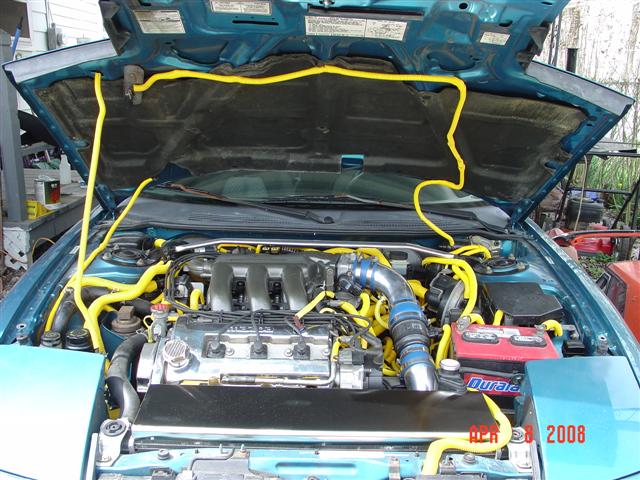 Engine bay with a V6 engine, yellow hoses, and a Duracell battery. Date stamp says April 28, 2008