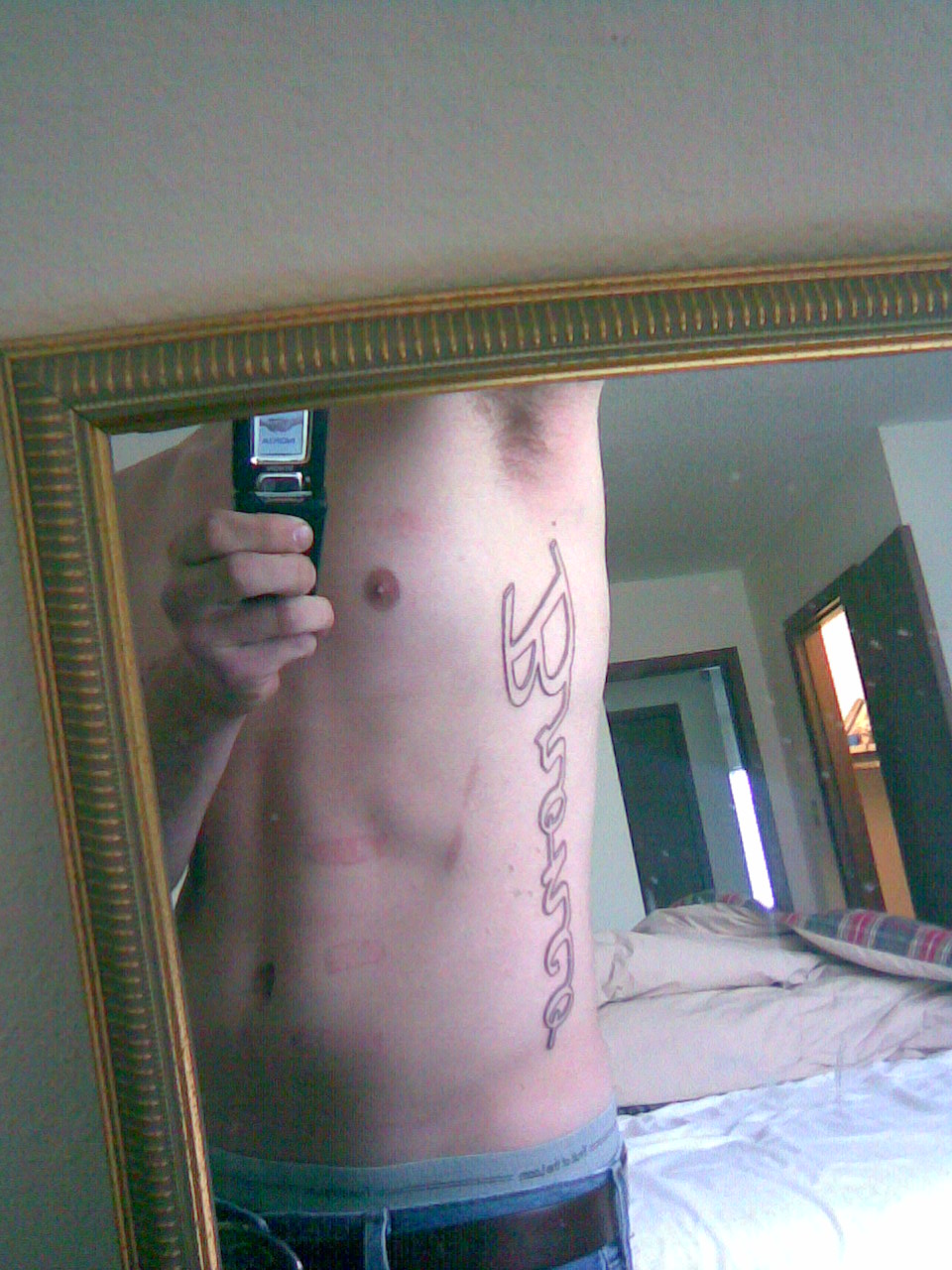 Mirror selfie of a person showing a vertical script rib tattoo