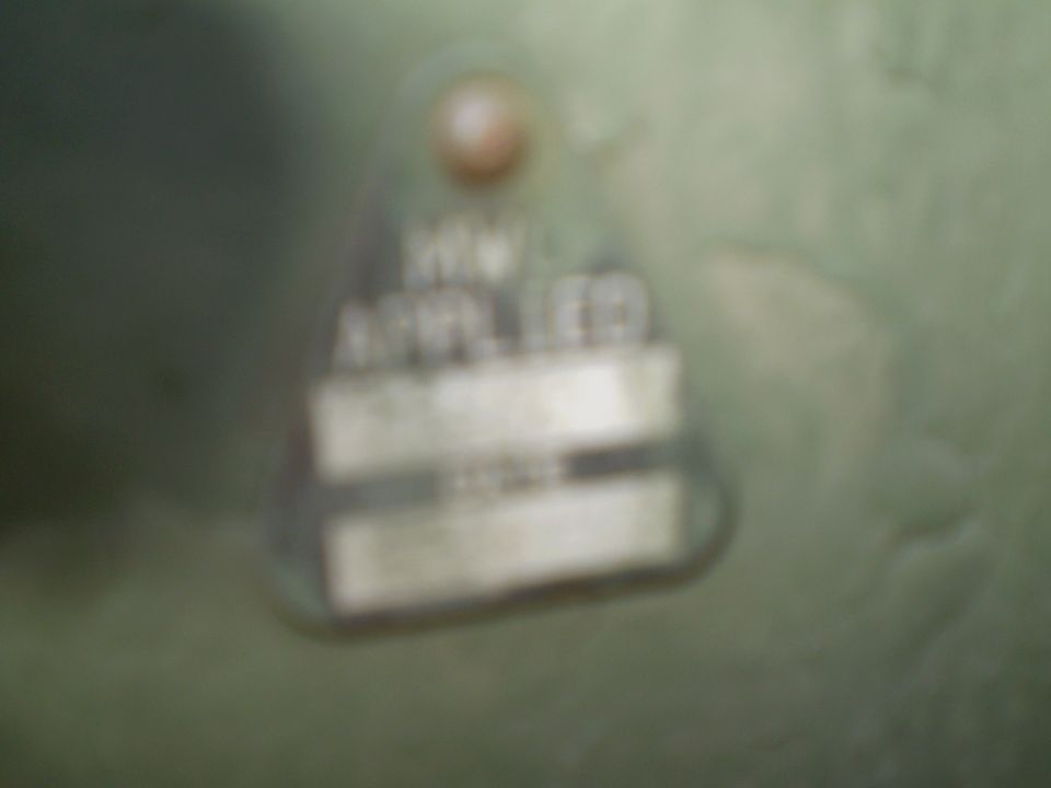 Blurry close-up of a riveted metal data plate on an olive-green vehicle panel