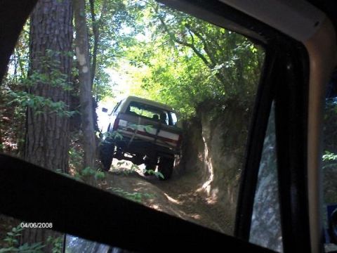 1987 Ford Bronco - A 1987 Ford Bronco navigates a narrow dirt trail surrounded by dense foliage.