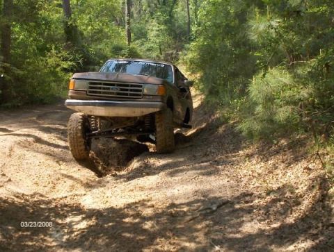 1987 Ford Bronco - 1987 Ford Bronco navigating a challenging off-road course in a wooded area.