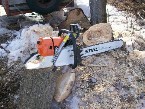 2000 Chevrolet Tahoe - A Stihl chainsaw is positioned on a log amidst snow and wood shavings, with a trailer wheel visible in the background.