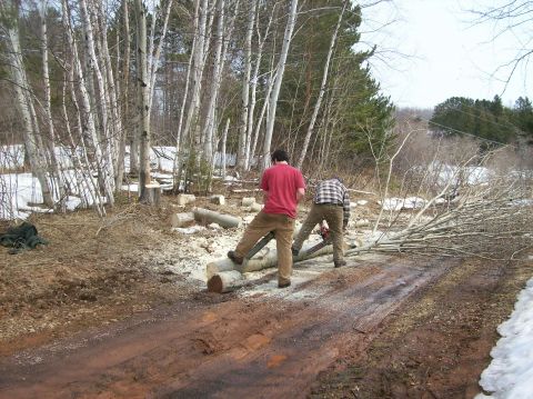 2000 Chevrolet Tahoe - Two men are working to cut logs with a chainsaw in a wooded area with snow on the ground.