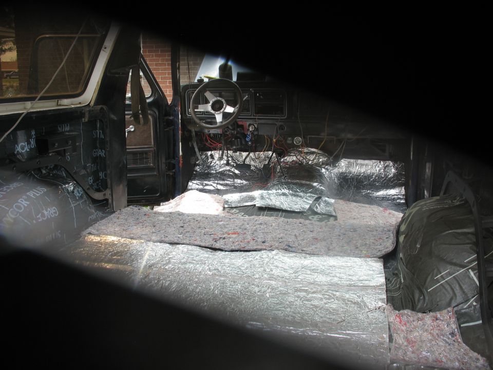 Vehicle interior with sound deadening material on floor and doors. Steering wheel and dashboard visible