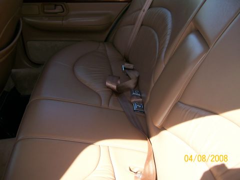 1995 Mercury Grand Marquis - Interior shot of a car's tan leather rear bench seat, showing the sculpted seatback, matching door panel with recessed pull handle and a br…