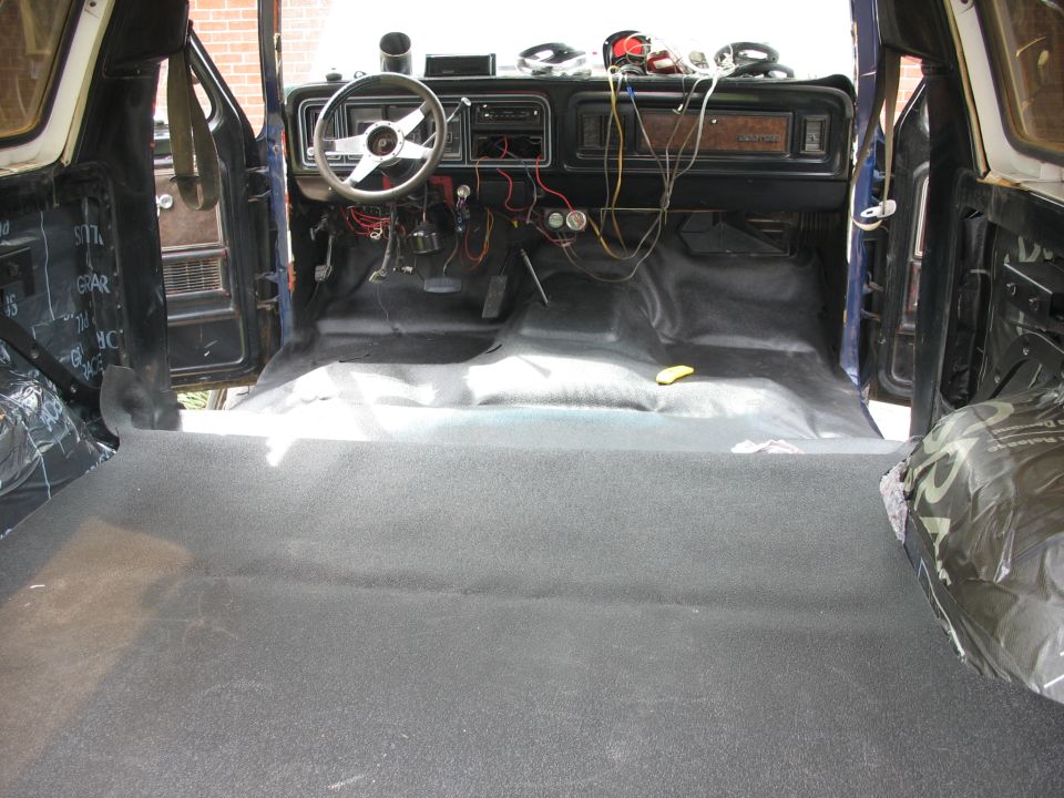 Interior of a classic truck or SUV, showing dashboard, steering wheel, and carpeted floor. Wiring is exposed on the dash
