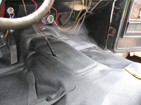1978 Ford Bronco - Interior floor of a vehicle showing new matting and exposed wiring near the dashboard.